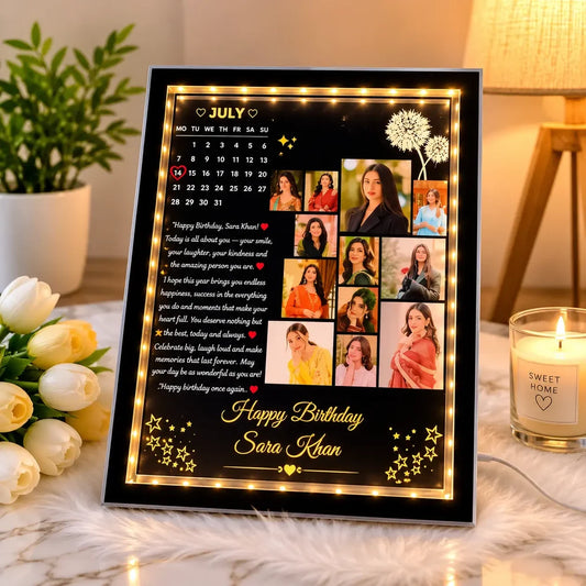 A personalized framed birthday photo board with built-in warm white LED lights, shown in a cozy home setting with a lit candle, flowers, and a lamp in the background.