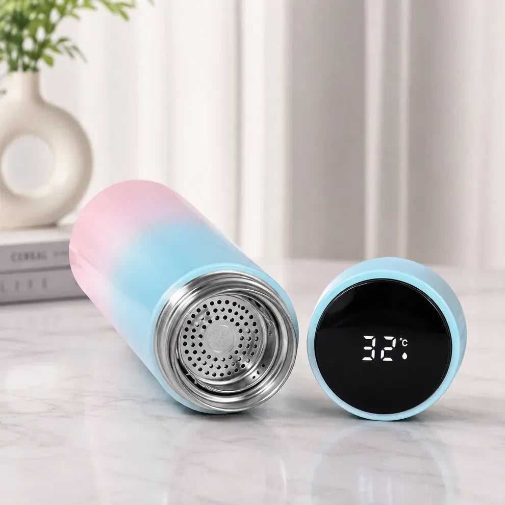 A pastel gradient travel tumbler shown open with its lid beside it on a light marble surface. The tumbler has a pink-to-blue gradient body, a stainless steel filter opening, and a light blue lid with a black digital temperature display reading 32°C.