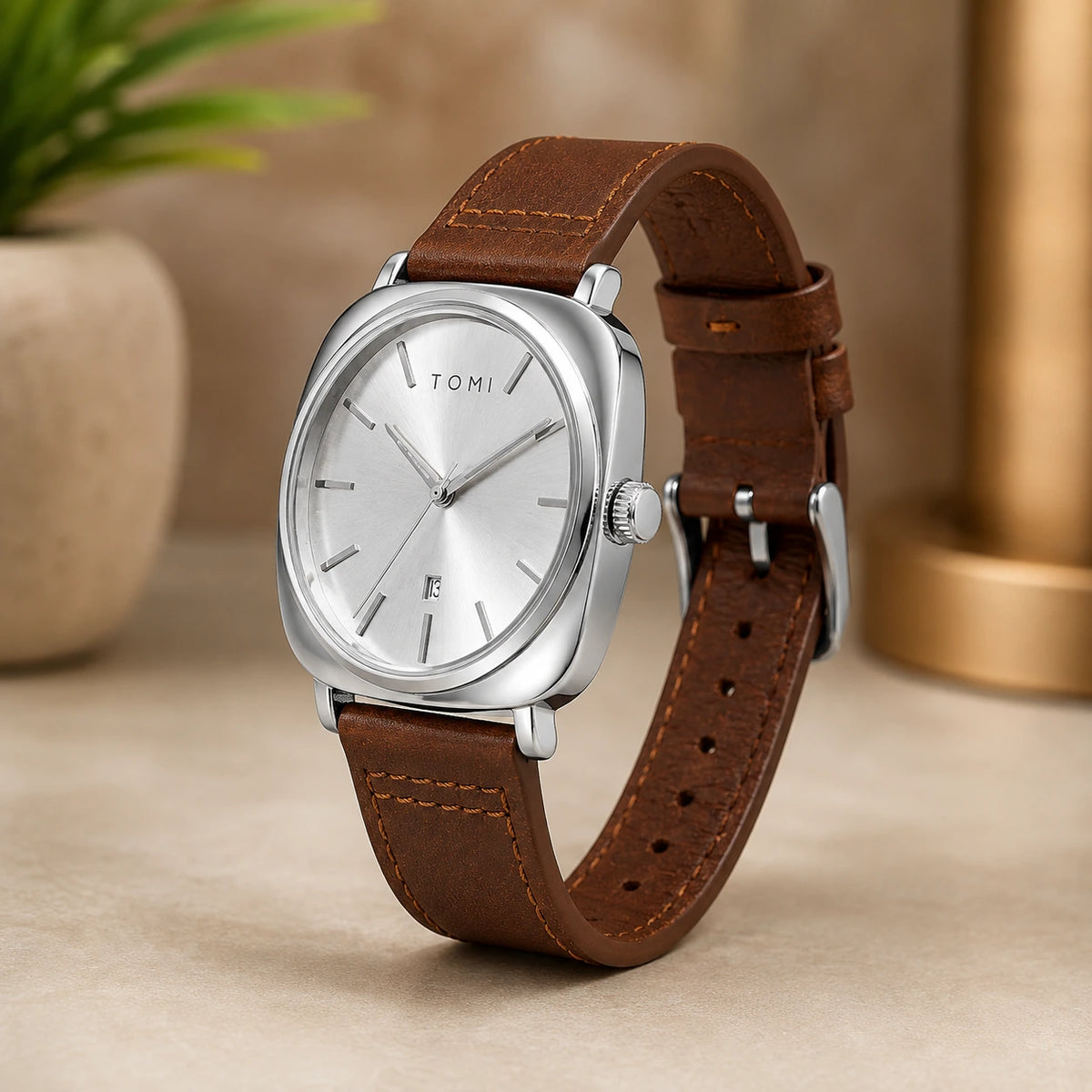 A Tumi analog watch with a silver-toned cushion-shaped case, silver dial, and brown leather strap, displayed on a beige surface with a blurred background.